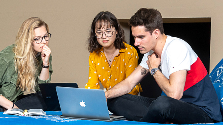 Studierende sitzen diskutierend vor Laptop